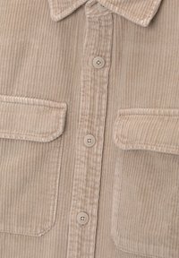 Camisa de pana beige, con una suave textura acanalada, dos bolsillos en el pecho, botones en la parte delantera y un cuello. Tejido suave y ligero.