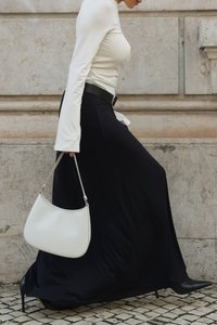 Zwarte maxirok gecombineerd met een getailleerde witte lange mouw top, zwarte riem en een witte handtas. Zwarte stilettohakken. Gestructureerde achtergrond.