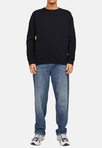 Sweatshirt bleu marine avec un col rond et des poignets côtelés, associé à un jean bleu clair à coupe décontractée et des baskets grises.