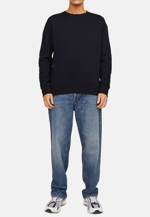 Marineblauwe sweatshirt met ronde halslijn en ribgebreide manchetten, gecombineerd met lichtblauwe ontspannen jeans en grijze sneakers.