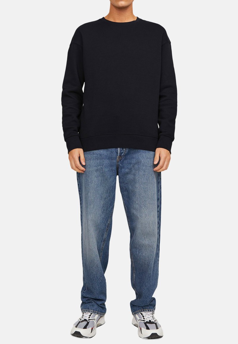 Sweatshirt bleu marine avec un col rond et des poignets côtelés, associé à un jean bleu clair à coupe décontractée et des baskets grises.