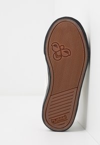 Braune Gummisohle mit strukturiertem Fischgrätenmuster und Logo. Schwarze Kante und leicht nach oben geneigt, die Material und Design präsentieren.