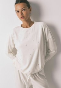 Lyse beige sweatshirt med lange ærmer, rund hals og små stjerne- og halvmåne-applikationer. Blødt stof og afslappet pasform.