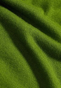 Strukturiertes grünes Gewebe mit einem weichen, gestrickten Aussehen. Das Material weist subtile Variationen in Farbe und Dichte auf, die Tiefe schaffen.