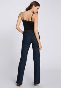 Schwarzes Top mit dünnen Trägern, kombiniert mit hochgeschnittenen, ausgestellten dunkelblauen Jeans, die eine glatte Textur und einen klassischen Denim-Stich aufweisen.