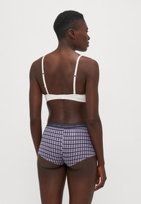 Weißes Bralette mit verstellbaren Trägern und Hakenverschluss, kombiniert mit lila gemusterten Shorts mit kontrastierendem elastischen Bund.