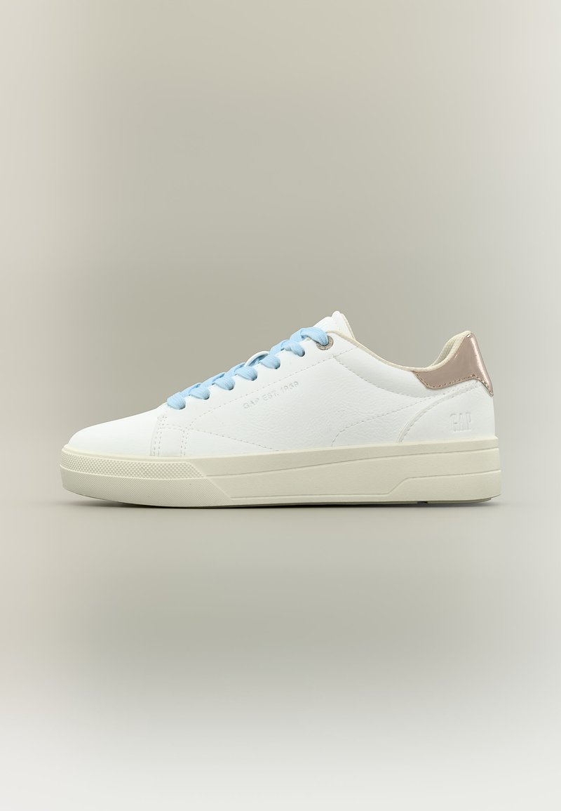 Baskets blanches basses avec lacets bleu clair et languette métallique beige au talon, sur un fond neutre.