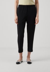 Pantalons noirs à taille élastique avec un design fuselé, ornés de manchettes roulées et d'une texture lisse, associés à des chaussures plates argent et noires.
