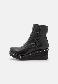 Botín negro de cuero con suela de cuña, que presenta costuras decorativas y remaches metálicos a lo largo de la base, además de un cierre de cremallera lateral.