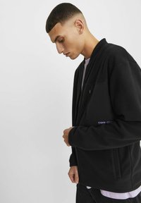 Black fleece bomber jacket with a zippered front, side pockets, and a chest pocket featuring "core depth" text in purple. Flat collar and cuffs.