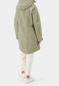 Manteau imperméable vert olive avec capuche, présentant une coupe droite, des fermetures à boutons-pression et un accent de logo à l'arrière. Tissu texturé.