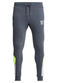Grijze sweatpants gemaakt van zacht materiaal, met een tailleband met trekkoord, een wit logo aan de voorkant en groene en grijze accenten aan de zijkanten.