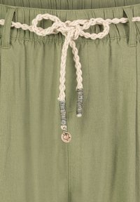 Light green pants featuring a braided cream drawstring with decorative metal accents. The fabric has a textured finish.