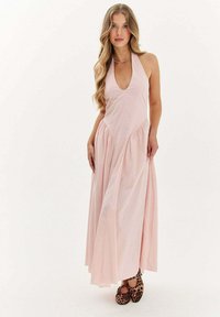 Ružová maxi šaty s halterným výstrihom, hlbokým V-výstrihom, zhrnutou sukňou a hladkou textúrou. Nosí sa s balerínkami s leopardím potlačou pre kontrast.