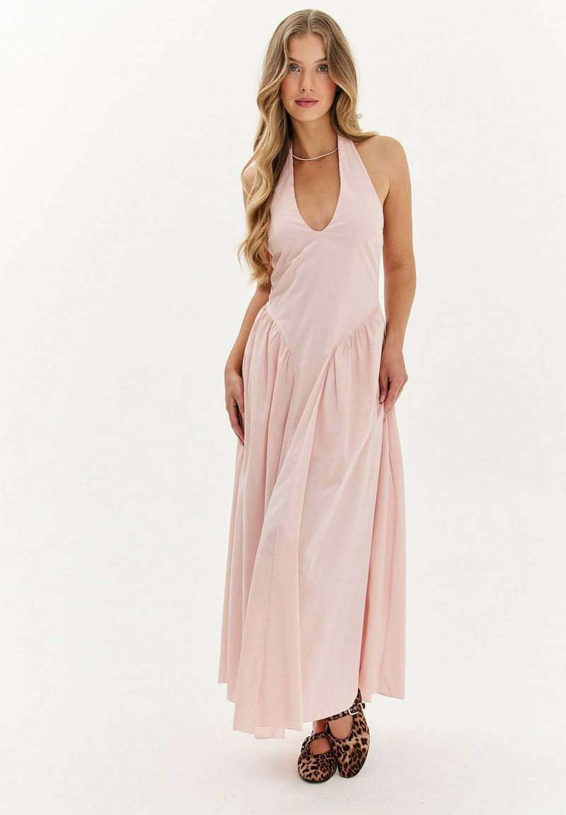 Ružová maxi šaty s halterným výstrihom, hlbokým V-výstrihom, zhrnutou sukňou a hladkou textúrou. Nosí sa s balerínkami s leopardím potlačou pre kontrast.