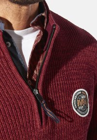 Burgunderfarbener strukturierter Pullover mit einem Viertel-Reißverschluss, gesticktem Logo und einem hellbraun karierten Stoff unter dem Kragen. Mit einem schwarzen Reißverschluss ausgestattet.