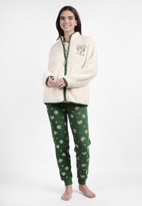 Chaqueta de forro polar crema con cremallera y ribete verde, con un diseño gráfico. Pantalones de pijama verdes con patrones de búhos y hojas, con puños elásticos.