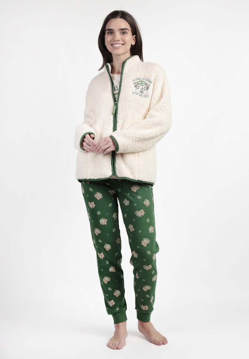 Chaqueta de forro polar crema con cremallera y ribete verde, con un diseño gráfico. Pantalones de pijama verdes con patrones de búhos y hojas, con puños elásticos.
