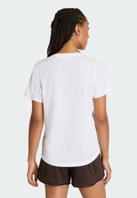 Biały T-shirt z krótkim rękawem, okrągłym dekoltem, gładką fakturą i luźnym krojem, w zestawieniu z brązowymi spodniami sportowymi.