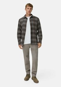 Geruite button-up shirt in grijstinten en bruin, over een wit T-shirt; gecombineerd met lichtgrijze broek en olijfgroene schoenen.