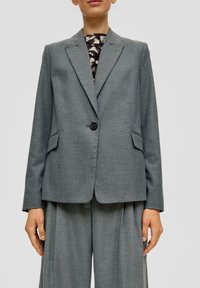 Šedý blazer s jedním knoflíkem, s klopovými límci a dvěma předními kapsami. Vyroben z texturované tkaniny, v kombinaci s volnými kalhotami.