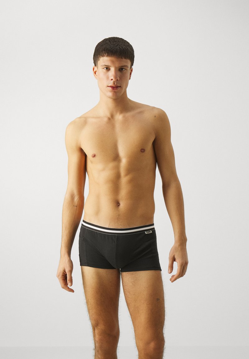Svarte boxer-shorts med en tettsittende design, elastisk midjebånd med to hvite striper, og en liten logo foran. Glatt stoffstruktur.