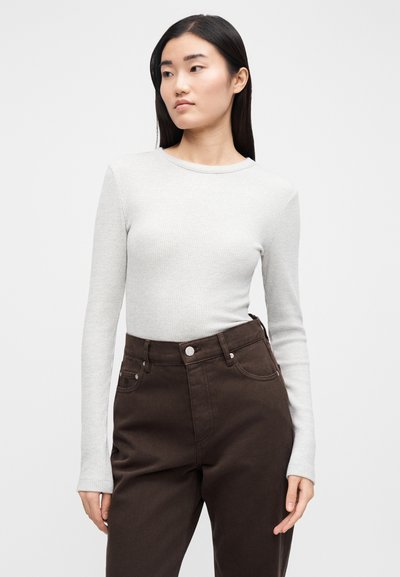 Világosszürke, hosszú ujjú felső bordázott anyagból, sötétbarna, magas derekú nadrággal párosítva, elején zsebekkel és gombos díszítésekkel.