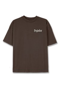 Hnedé bavlnené tričko s kruhovým výstrihom, krátkymi rukávmi a malým bielym logom "Pegador" na hrudi. Hladká textúra, voľný strih.