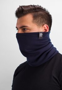 Navy neck gaiter made of soft, stretchy fabric, with a smooth texture and a small logo tag on the side. Worn around the neck and face.