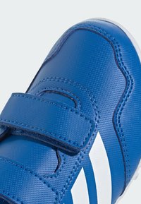 Blue sneaker with textured synthetic upper, featuring two Velcro straps and three white stripes on the side. Rounded toe and contrasting sole.