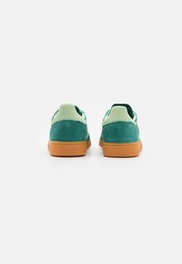 Zelené semišové tenisky se světle zeleným akcentem na patě a podrážkou z gumové pryže. Mají elegantní, nízký střih a texturovaný povrch.