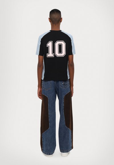 Camiseta de manga corta negra y azul claro con el número 10 en rosa en la espalda, combinada con pantalones vaqueros de pernera ancha con acentos marrones.