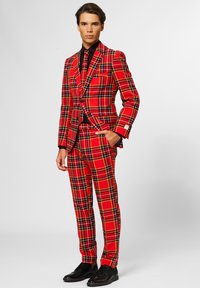 Red plaid suit featuring a fitted blazer and trousers, accented with black lines. Paired with a black shirt and shoes.