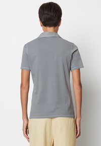 Grå polo skjorta med krage och korta ärmar, med en slät textur och kontrasterande sömdetaljer, visad från baksidan.