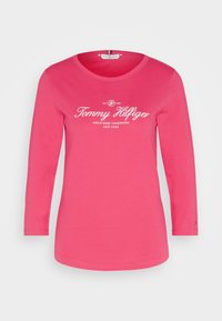 T-shirt a maniche lunghe rosa in cotone. Presenta un colletto girocollo e il logo stampato "Tommy Hilfiger" in bianco sulla parte centrale del petto.