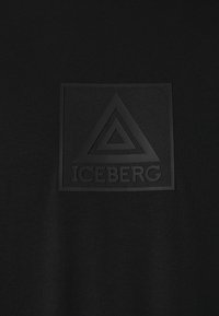Camiseta de algodón negra con un logo de goma negra en relieve con un diseño triangular y la palabra "ICEBERG" en la zona del pecho.