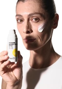 Crema Invisibile Hydrasun SPF 50 in una bottiglia bianca a pompa, con una crema bianca liscia applicata sulla guancia del modello, con etichettatura chiara.