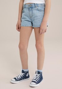 Traperice kratke hlače s vertikalnim bijelim prugama, visokog struka, izrezani rub, u kombinaciji s plavim visokim tenisicama i svijetloplavim čarapama do gležnja.