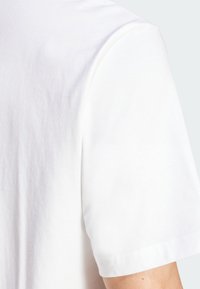 Witte katoenen t-shirt met korte mouwen, met een gladde textuur en een ronde halslijn. Naaddetails bij de schouder en de mouwrand.