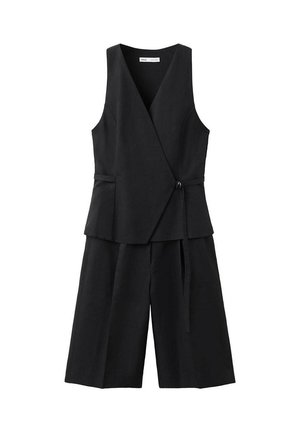 Chaleco negro sin mangas con cierre cruzado y lazo lateral combinado con pantalones cortos culotte de pierna ancha a juego sobre fondo blanco.