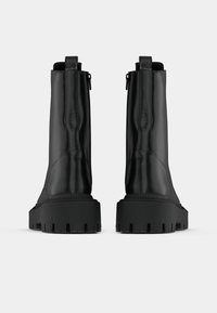 Black ankle boots with a smooth leather finish, chunky rubber sole, and back zipper. Features a rounded toe and textured accents.