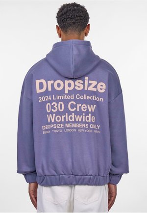 Purple hoodie with oversized fit, featuring a kangaroo pocket, ribbed cuffs, and back graphic text in light pink indicating a limited collection.