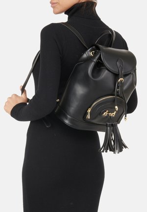 Zaino in pelle nera con forma arrotondata, hardware dorato, tasca con zip e accentuazione con frange. Texture liscia, chiusura a cordoncino.