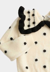 Crèmekleurige gebreide trui met zwarte stippen, een gerimpelde kraag met zwarte rand en pompon-details, en geribbelde manchetten.