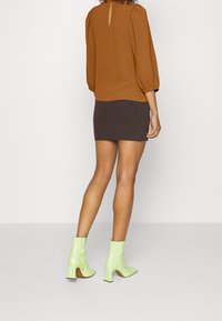 Haut marron à manches bouffantes avec un dos en clé, associé à une mini jupe grise à côtes. Le mannequin porte des bottines brillantes vert lime avec des talons à bloc.