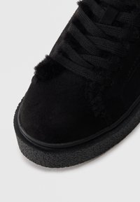 Sneakers en daim noir avec une surface texturée, bout rond, semelle en caoutchouc épaisse et lacets proéminents, dotés d'accents doux et pelucheux le long du dessus.