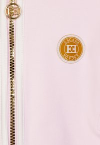 Giacca rosa con zip dorata, caratterizzata da un logo circolare arancione e bianco di Escada sul davanti. Tessuto a trama liscia.