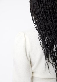 White knitted sweater with puffed shoulder detail, soft texture, and long dark braided hair cascading down the back.