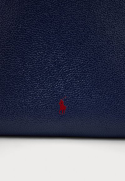 Τσαντάκι ώμου από δέρμα σε ναυτικό μπλε με υφή και έντονο κόκκινο κεντητό λογότυπο ενός αναβάτη επάνω σε άλογο.