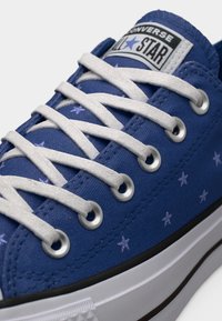 Μπλε αθλητικό παπούτσι Converse All Star με λευκά κορδόνια, μικρά αστέρια, μεταλλικές οπές και λευκή λαστιχένια σόλα με μαύρη ρίγα.